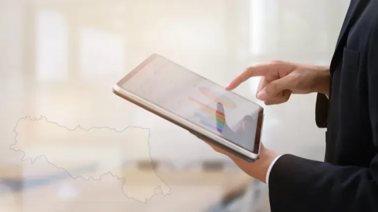 Una persona in giacca consulta un grafico su tablet, con la sagoma dell'Emilia-Romagna in filigrana